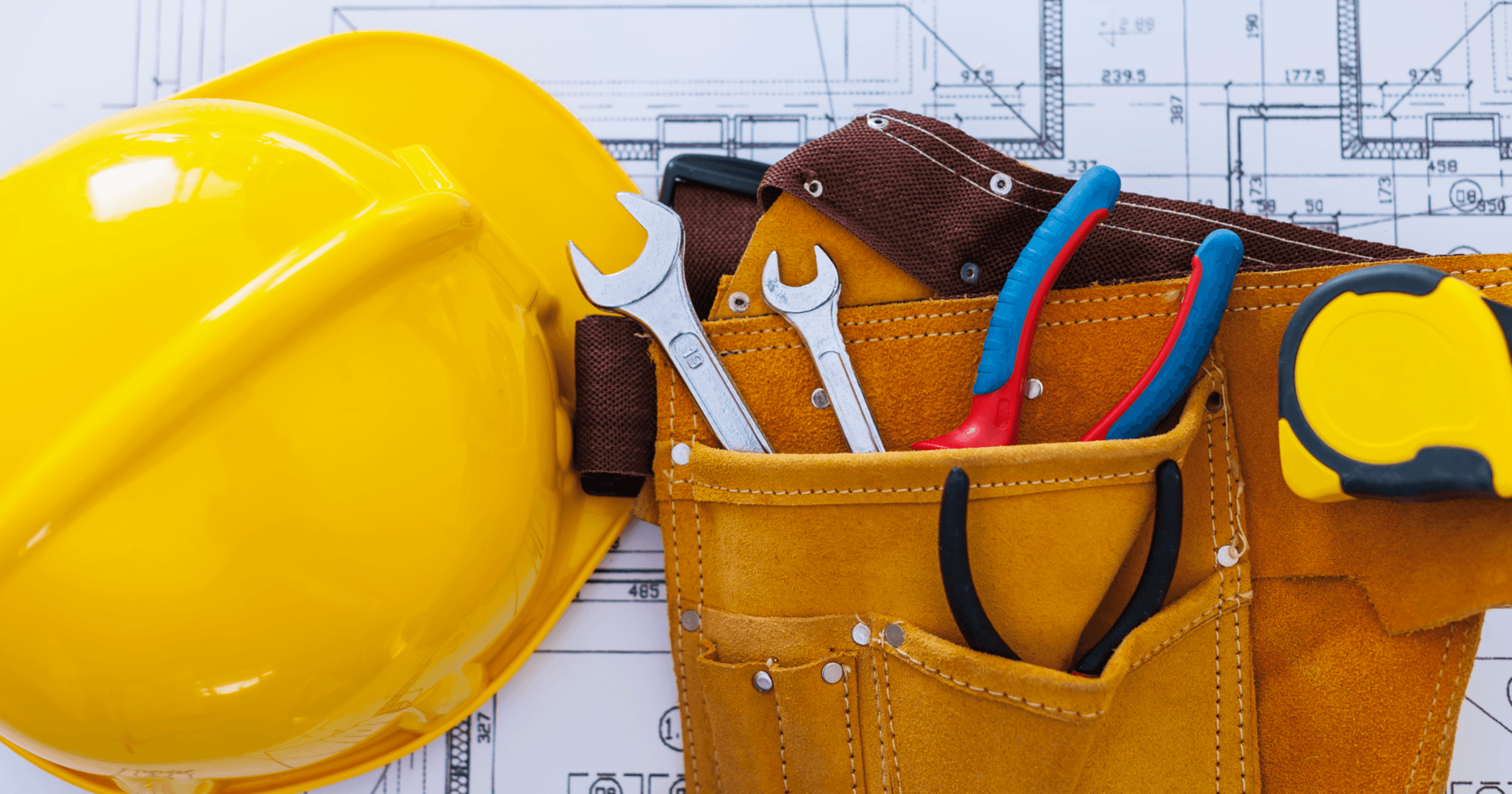 Yellow hard hat and tool belt with wrenches and pliers on construction blueprints