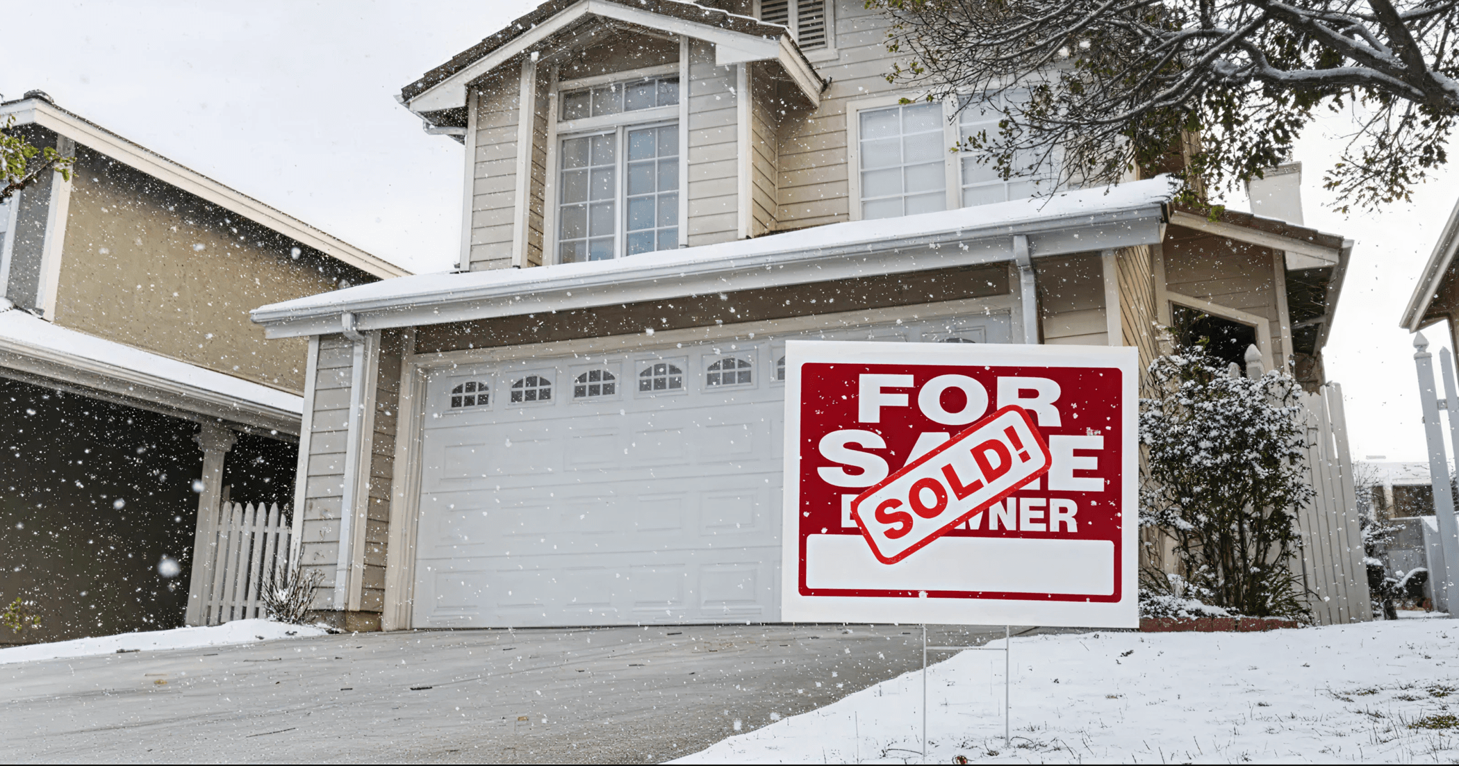 For Sale sign with SOLD stamp in front of beige house during snowfall